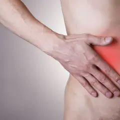 Dłoń uciska bolące miejsce po prawej stronie pod żebrami, gdzie skóra jest zaczerwieniona.