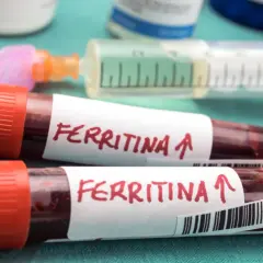 Dwie probówki z krwią oznaczone "Ferritina" i strzałką w górę, sugerującą podwyższony poziom, obok strzykawki.