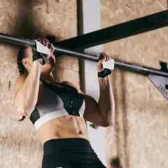 Kobieta wykonuje podciąganie na drążku podczas treningu crossfit. Silne ramiona i brzuch świadczą o jej determinacji.