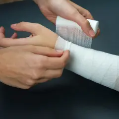 Opatrywanie rany na przedramieniu. Biały bandaż owija się wokół kończyny, zapewniając wsparcie.