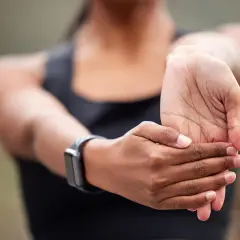 Kobieta rozciąga nadgarstek, ćwicząc jak wzmocnić nadgarstki. Na ręce ma smartwatch.
