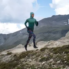 Kobieta w sportowym stroju biegnie po górskim szlaku, utrzymując rytmiczną kadencję bieganie.