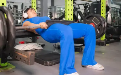 Kobieta w niebieskim stroju wykonuje hip thrust, jedno z najlepszych ćwiczeń na pośladki, z obciążeniem na sztandze.