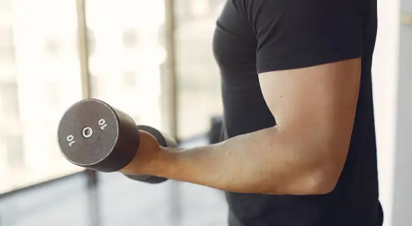Mężczyzna ćwiczy biceps z hantlem 10 kg. Zastanawiasz się, ile serii na biceps w tygodniu jest optymalne?