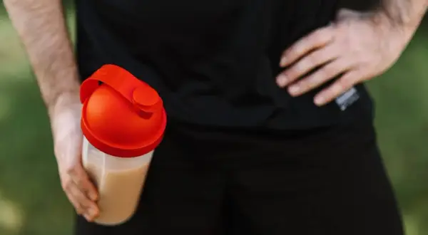 Mężczyzna trzyma shaker z napojem. Czy kreatyna zatrzymuje wodę? To pytanie nurtuje wielu sportowców.
