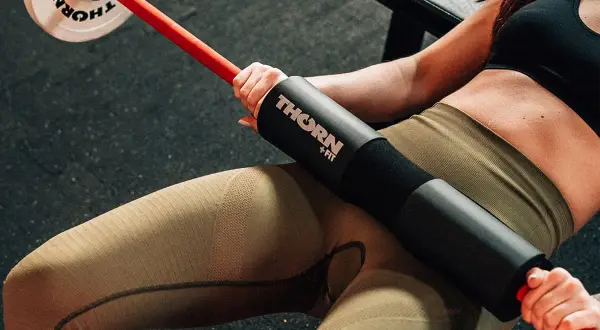 Kobieta wykonuje hip thrust w domu z gryfem i obciążeniem.