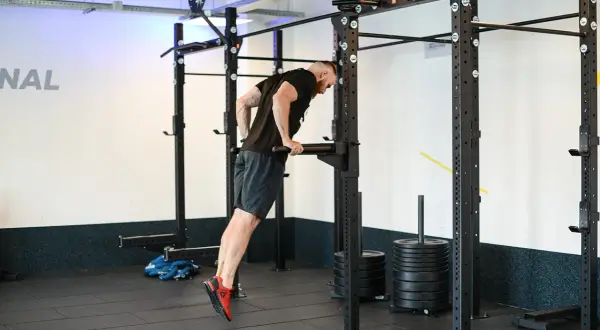 Mężczyzna wykonuje ćwiczenie na dipy na triceps, angażując mięśnie ramion.