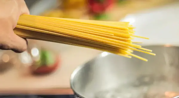 Dłoń trzymająca spaghetti nad gotującą się wodą. Zastanawiasz się, jaki makaron ma najmniej kalorii?