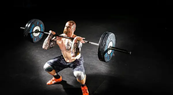 Mężczyzna z tatuażami wykonuje rack pull z ciężarem.