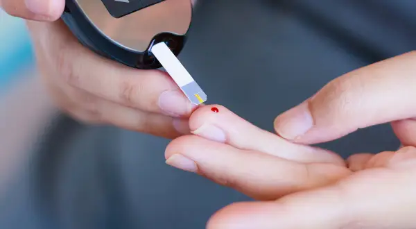 Osoba mierzy poziom glukozy glukometrem. Zrozumienie, dlaczego cukier rośnie bez jedzenia, jest kluczowe dla diabetyków.