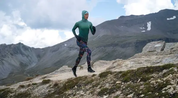Kobieta w sportowym stroju biegnie po górskim szlaku, utrzymując rytmiczną kadencję bieganie.