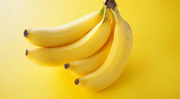 Pęczek żółtych bananów na żółtym tle. Zastanawiasz się, ile banan ma kalorii?