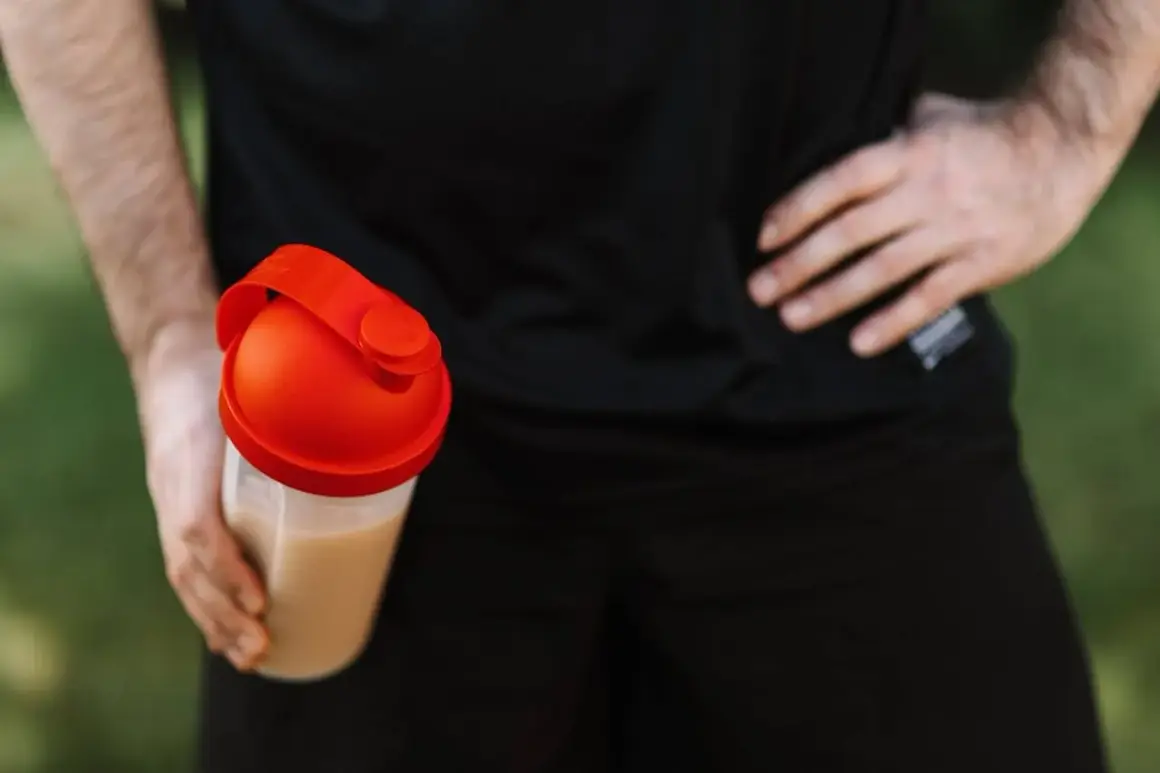 Mężczyzna trzyma shaker z napojem. Czy kreatyna zatrzymuje wodę? To pytanie nurtuje wielu sportowców.