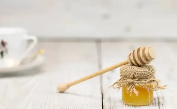Mały słoiczek miodu z drewnianą chochlą, idealny do słodzenia herbaty. Łyżka miodu kcal to tylko dodatek do pysznego smaku.