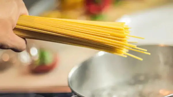 Dłoń trzymająca spaghetti nad gotującą się wodą. Zastanawiasz się, jaki makaron ma najmniej kalorii?