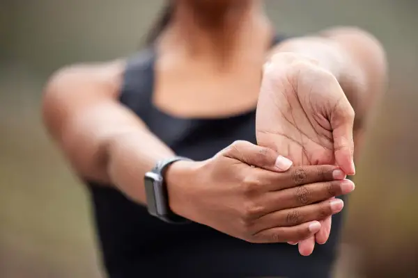 Kobieta rozciąga nadgarstek, ćwicząc jak wzmocnić nadgarstki. Na ręce ma smartwatch.