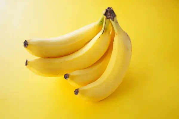 Pęczek żółtych bananów na żółtym tle. Zastanawiasz się, ile banan ma kalorii?