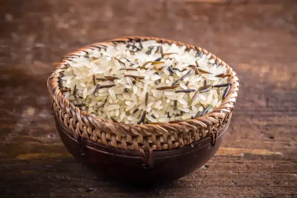 Mieszanka ryżu basmati i dzikiego ryżu w plecionej misce na drewnianym tle.